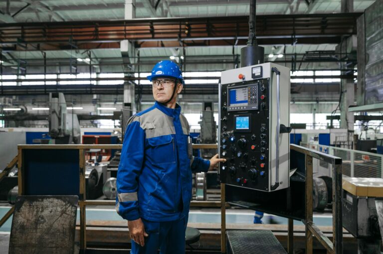 Male factory worker in protective gear operates machinery indoors.