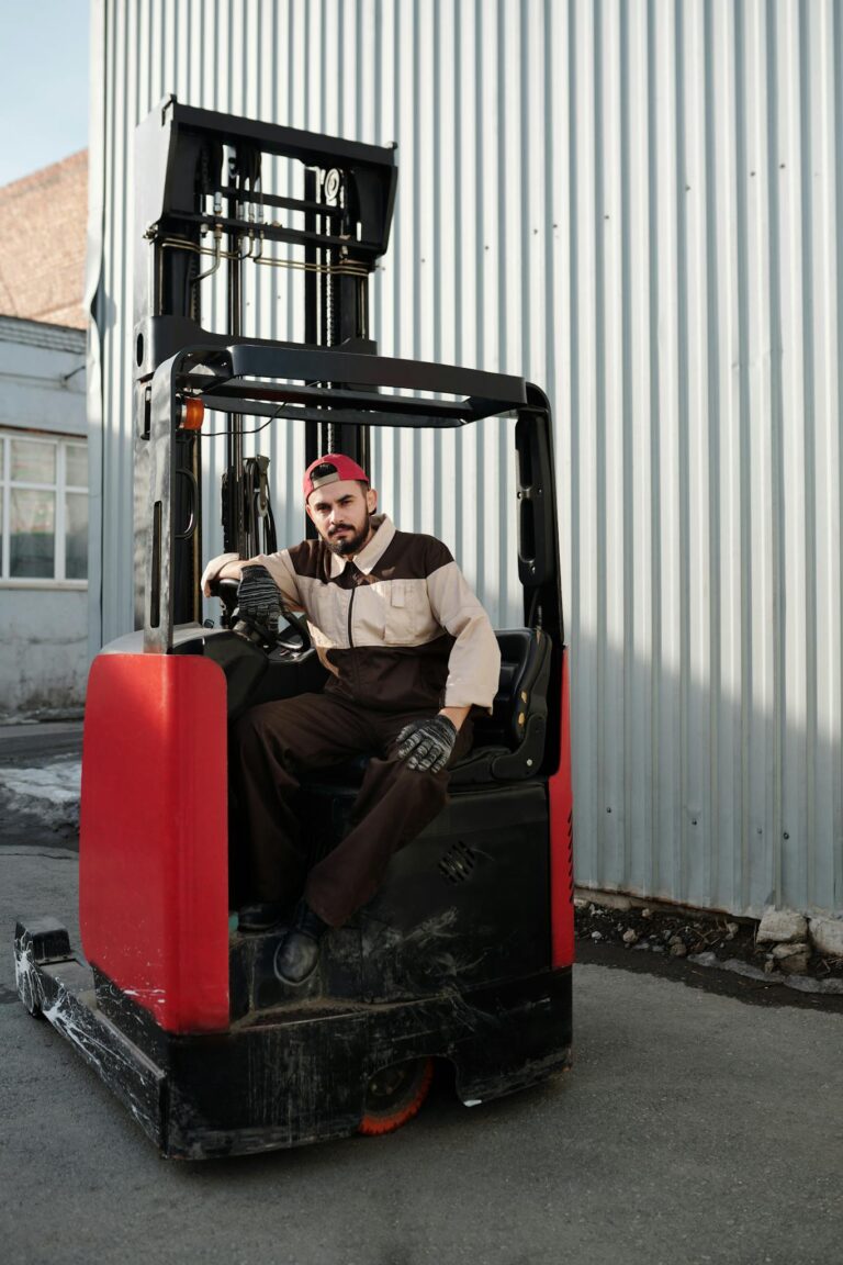 Male forklift operator working outdoors near industrial building.