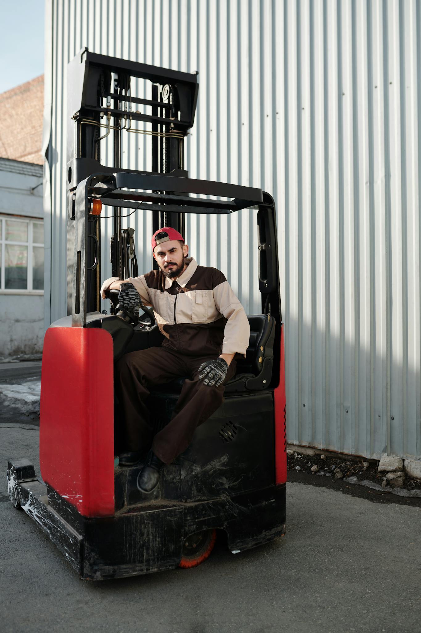 Male forklift operator working outdoors near industrial building.
