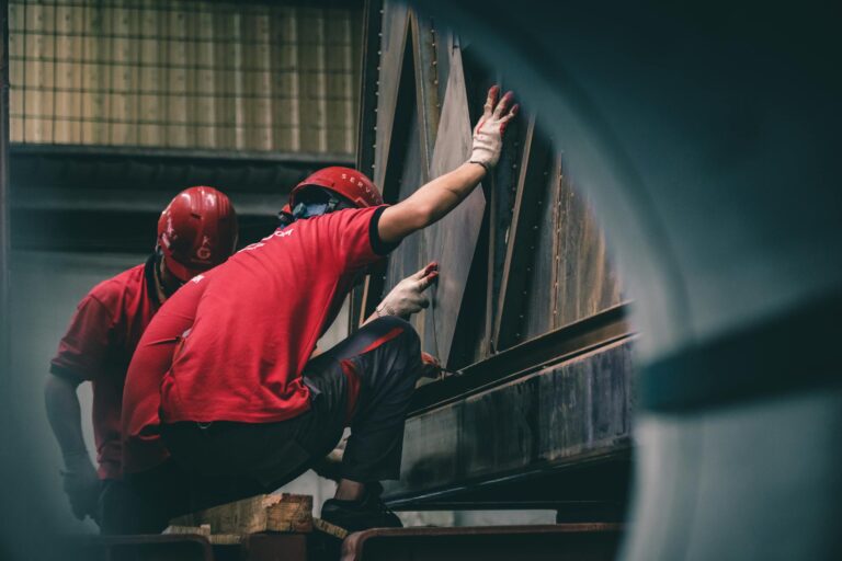 Workers in red uniforms and helmets inspecting industrial machinery.